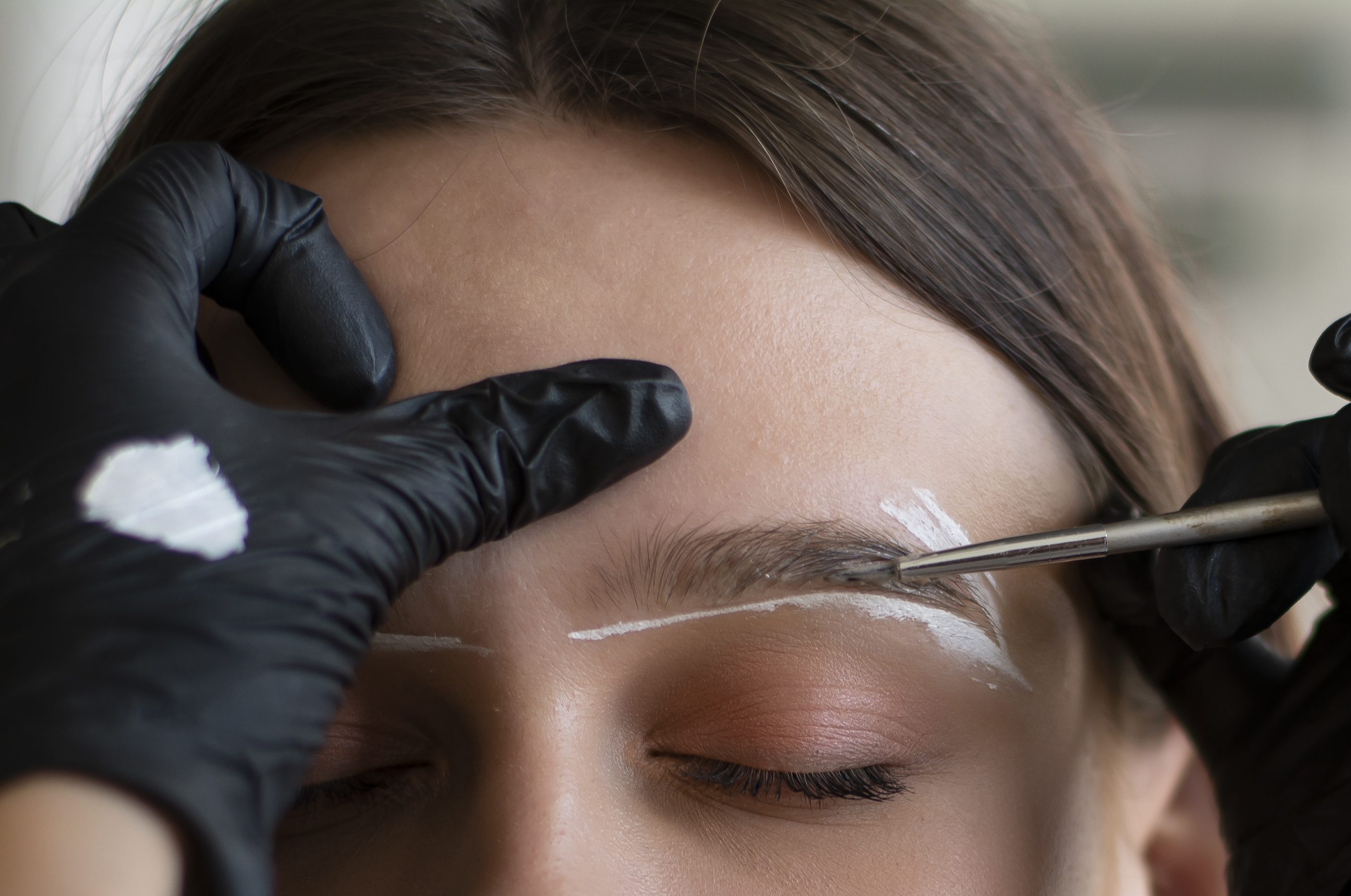 A person getting eyebrow shaping with a brush and white pencil marks.